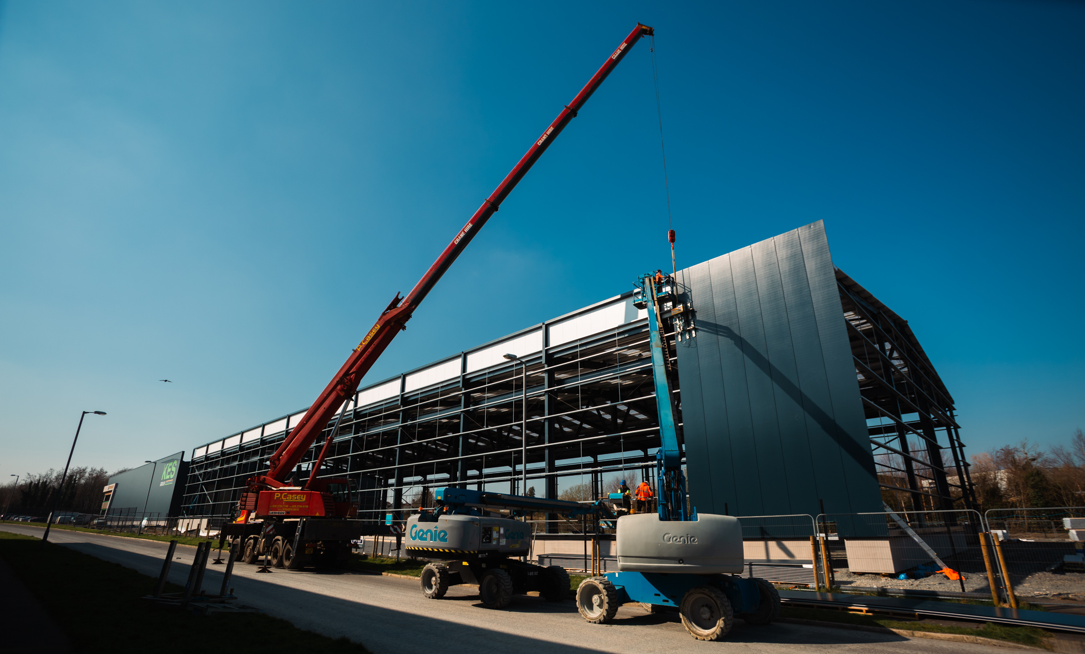 Members of the KESGroup team working on the construction of Phase three. There is a cran onsite and a man in a cherry picker installing wall panels.